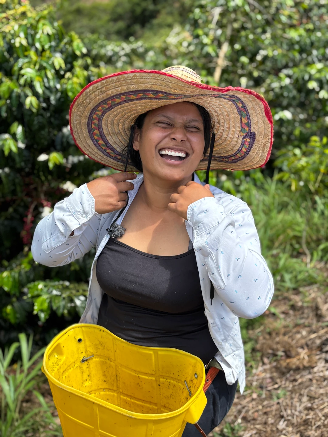 Caficultora sonriendo en su finca con sombrero y canasto de cosecha